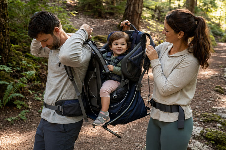 parents switching off wearing baby hiking carrier on trail