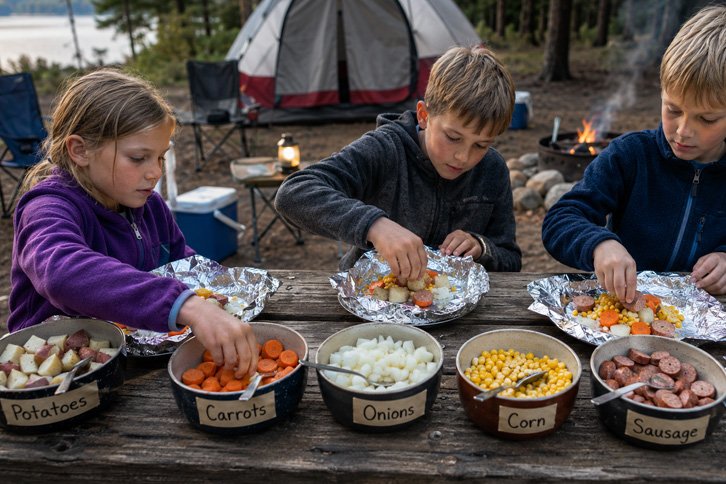 kids making foil packet camping meals at picnic table